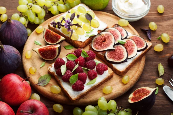 Nützliche Bio-Sandwiches mit Diät-Käsecreme, Himbeeren, grünen Trauben und Feigen auf einem runden Holzschneidebrett. neben Äpfeln, Trauben und Feigen. Selektive Schärfe. Nahaufnahme — Stockfoto