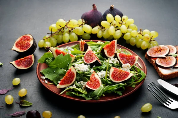 Nyttig kost sallad från ruccola, fikon, getost och olivolja. Nära den gröna druvor och fikon. Läcker ekologisk hemlagad maträtt. — Stockfoto