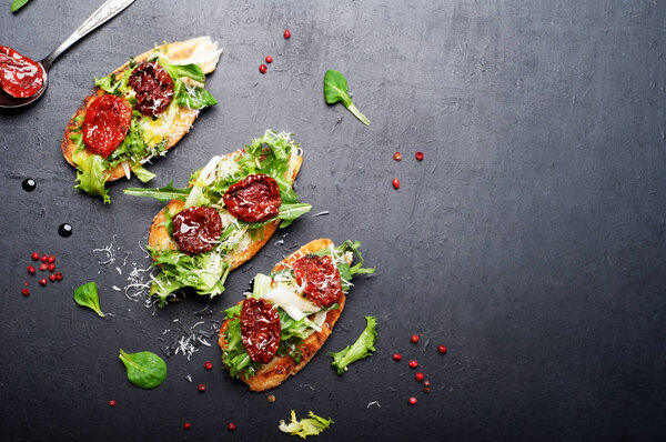 'Bruschetta' (sandwich) with toast, mix of Italian herbs (iceberg, breeze, mung bean, arugula) and dried tomatoes on a dark surface. Italian food. Vegetarian, vegan concept.