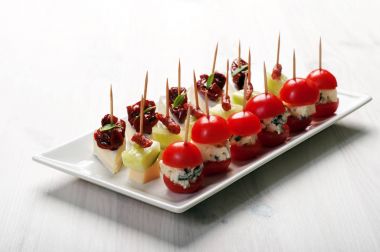 Kanepe (mini sandviç) yumuşak peynir, mavi peynir, güneş kurutulmuş domates, sosis, domates ve fesleğen ile beyaz bir plaka üzerinde bırakır. Rafine bir aperatif. Avrupa mutfağı. Makro çekim. Metin için yer