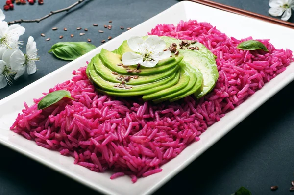 Rosafarbener Reis mit Avocadoscheiben auf rechteckigem Teller auf schwarzem Hintergrund. nützliche kalorienarme Fertiggerichte. vegetarisches, veganes Konzept. Makroaufnahmen, selektive Schärfe. — Stockfoto