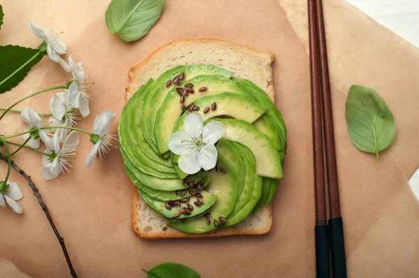 Sandwich med avokado och lin frön på pergament. Nästa blad en gren med körsbärsblommor och basilika. En nyttig kalorisnål redo maträtt. Vegetarisk, vegan koncept. Östra rätter — Stockfoto