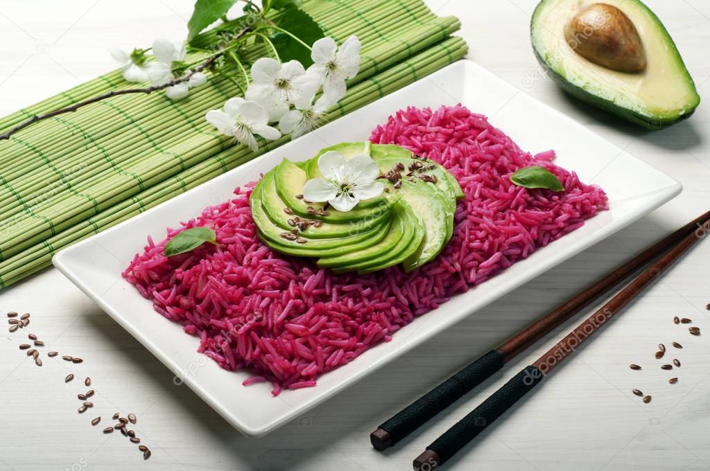 Pink rice with slices of avocado in a rectangular plate on white wooden background. Macro shooting. Selective sharpness. A useful low calorie ready dish. Vegetarian, vegan concept. Eastern cuisine