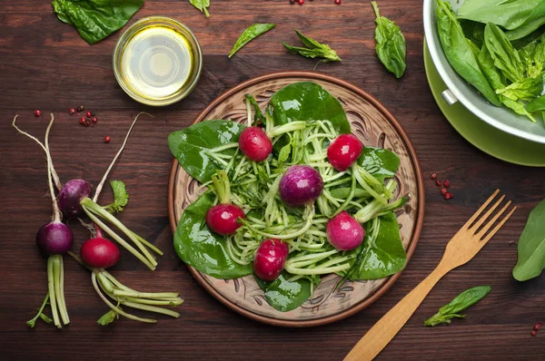 Ensalada de hojas de espinaca, pepino picado y un colorido rábano en un plato de arcilla marrón sobre un fondo de madera oscura. Un plato útil bajo en calorías listo. Vegetariano, concepto vegano —  Fotos de Stock