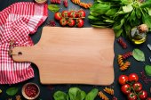 Картина, постер, плакат, фотообои "background. italian food. multicolored pasta, tomatoes, spinach, basil leaves and olive oil on a dark surface. in the center of the image is wooden cutting board on which you can arrange dish or text", артикул 153770966