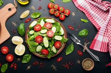Karanlık bir arka plan üzerinde düşük kalorili diyet vegan salata tabağı. Salata dan ıspanak yaprakları, domates ve salatalık dilimleri. Yararlı diyet yemeği. Vejetaryen, vegan kavramı