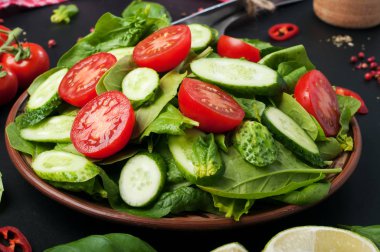 Karanlık bir arka plan üzerinde düşük kalorili diyet vegan salata tabağı. Salata dan ıspanak yaprakları, domates ve salatalık dilimleri. Yararlı diyet yemeği. Vejetaryen, vegan kavramı