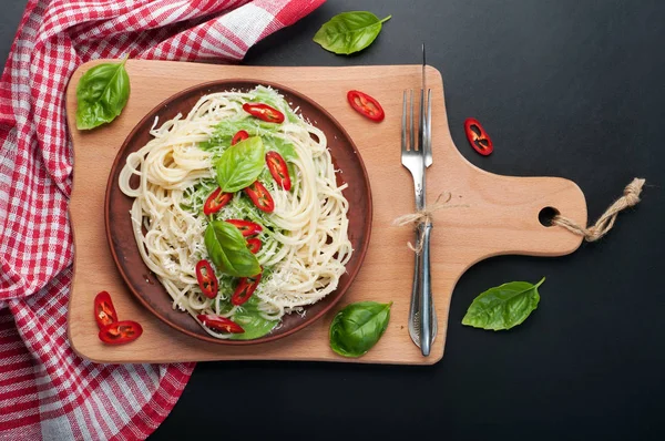 Pasta (spaghetti) met basilicum en roomsaus, geraspte kaas en stukken van hete peper op een bruin kleiplaat op een snijplank. Donkere achtergrond. Italiaans eten. Vegetarische concept. Lekkere en gezonde lunch — Stockfoto