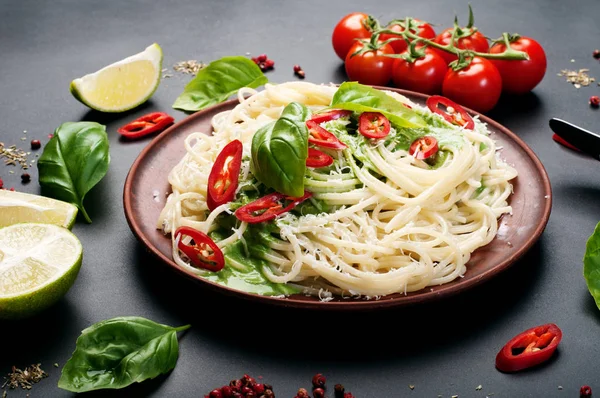 Pasta (spaghetti) met basilicum en roomsaus, geraspte kaas en stukken van hete peper op een bruin kleiplaat op een donker oppervlak. Italiaans eten. Vegetarische concept. Lekkere en gezonde lunch — Stockfoto