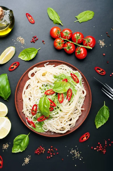 Paste (spaghete) cu sos de busuioc și smântână, brânză rasă și bucăți de piper fierbinte pe o placă maro argilă pe o suprafață întunecată. Mâncare italiană. Conceptul vegetarian. Prânz delicios și sănătos — Fotografie, imagine de stoc