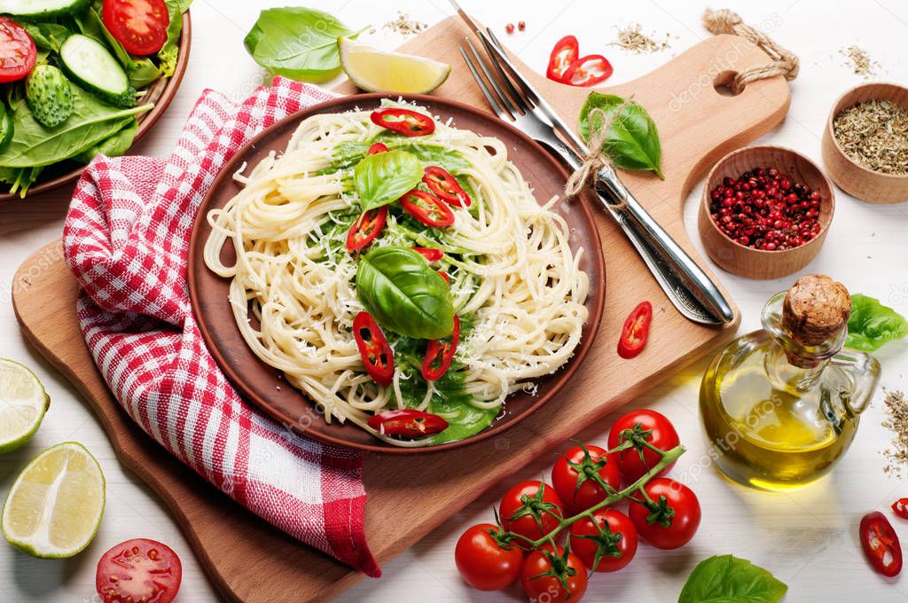 Pasta (spaghetti) with basil and cream sauce, grated cheese and pieces of hot pepper on a clay brown plate on a  cutting board. White background. Italian food. Vegetarian concept. Delicious and healthy lunch