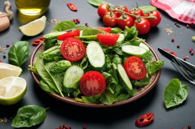 Karanlık bir arka plan üzerinde düşük kalorili diyet vegan salata tabağı. Salata dan ıspanak yaprakları, domates ve salatalık dilimleri. Yararlı diyet yemeği. Vejetaryen, vegan kavramı