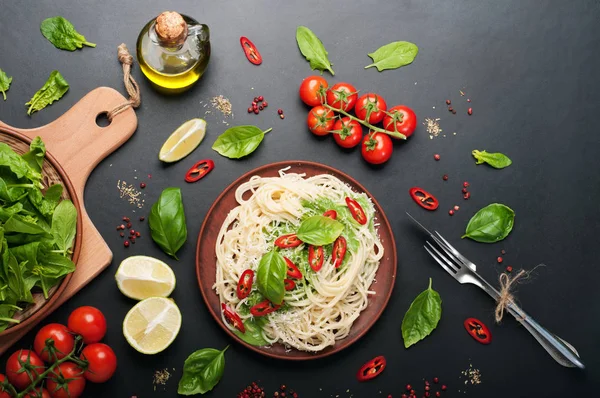 Pasta (spaghetti) con basilico e crema di salsa, formaggio grattugiato e pezzetti di peperoncino su un piatto di argilla marrone su una superficie scura. Cibo italiano. Concetto vegetariano. Pranzo delizioso e sano — Foto Stock