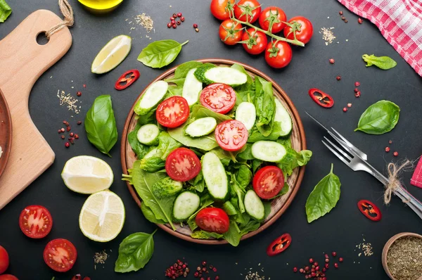Placa de salada vegan dietética de baixa caloria em um fundo escuro. Salada de folhas de espinafre, tomates cereja e fatias de pepino. Jantar dietético útil. Vegetariano, conceito vegan — Fotografia de Stock