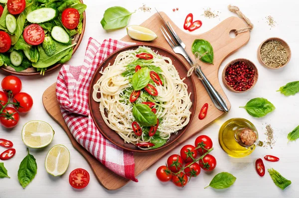 Pasta (spaghetti) con basilico e crema di salsa, formaggio grattugiato e pezzetti di peperoncino su un piatto di argilla marrone su un tagliere. Sfondo bianco. Cibo italiano. Concetto vegetariano. Pranzo delizioso e sano — Foto Stock