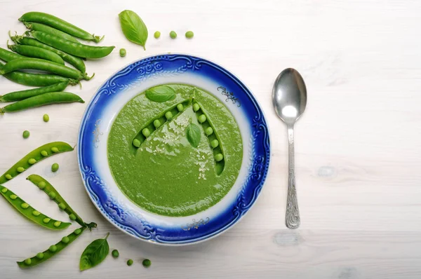 Puré de sopa dietética con guisantes verdes en un plato con un borde azul en una tabla de madera blanca. Cocina casera dietética baja en calorías. Vegetariano, concepto vegano —  Fotos de Stock