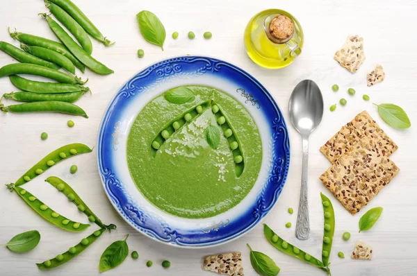 Puré de sopa dietética con guisantes verdes en un plato con un borde azul en una tabla de madera blanca. Cocina casera dietética baja en calorías. Vegetariano, concepto vegano —  Fotos de Stock