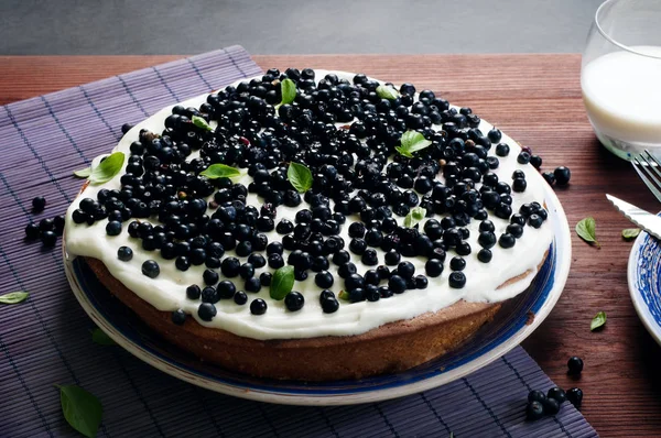Cake (biscuit) with cream and blueberries on a blue plate on a brown wooden background. Light summer home cake