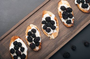 Bruschetta (tost baget üzerinden) krem peynir ve bir kahverengi ahşap tahta üzerinde böğürtlen ile