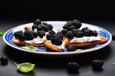 Krem peynir ve karanlık bir yüzey üzerinde bir tabakta böğürtlen ile tost. Mevsim yaz sandviç. 