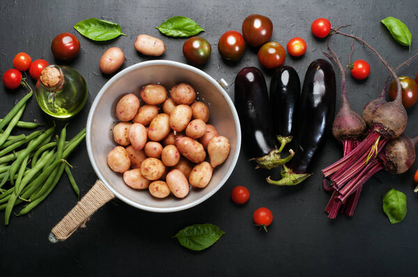 Fresh organic vegetables such as carrots, beets, asparagus beans, tomatoes, eggplants, potatoes and basil leaves  on a dark surface. Vegetarian, vegan concept