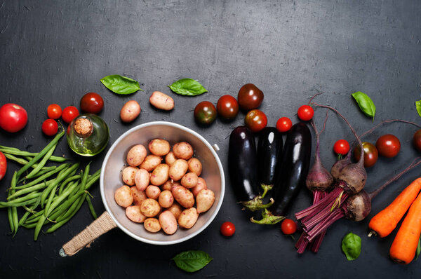 Vegetable background. Fresh organic vegetables such as carrots, beets, asparagus beans, tomatoes, eggplants, potatoes and basil leaves  on a dark surface. Place for text 