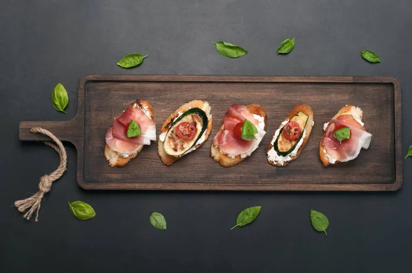 Krem peynir, jambon, kiraz domates, fesleğen yaprağı, kabak ve ahşap kesme tahtası üzerinde ızgara patlıcan ile tost. Lezzetli taze pişmiş snack (ev yapımı sandviç). Metin için yer