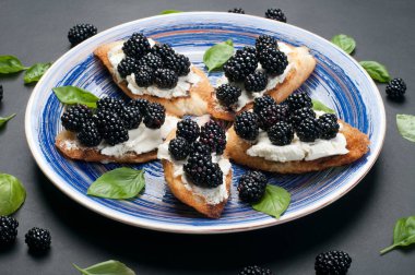 Krem peynir ve karanlık bir yüzey üzerinde mavi plaka üzerinde böğürtlen ile tost. Mevsim yaz sandviç. Makro çekim