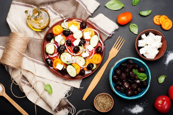 Mediterrane gerechten. Salade van tomaten, komkommers, paarse uien en gedroogde olijven op een bruin bord op een donkere achtergrond. Fusion Griekse salade. Lekker en gezond seizoensgebonden schotel. — Stockfoto