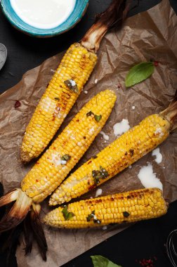 Zeytinyağı, biber, tuz ve fesleğen parşömen kağıt üzerine karanlık bir yüzey üzerinde Mısır pişmiş. Vejeteryan, vejeteryan menü