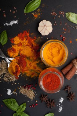 Parlak baharatlar, baharat ve otlar (zerdeçal, kırmızı biber, pembe biber, tarçın, fesleğen, kekik, anason ve sarımsak) karanlık bir tahta üzerinde