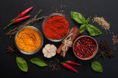 Parlak baharatlar, baharat ve otlar (zerdeçal, kırmızı biber, pembe biber, tarçın, fesleğen, kekik, anason ve sarımsak) karanlık bir tahta üzerinde