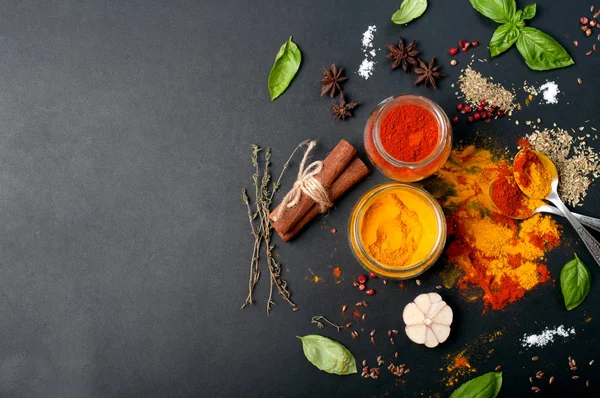 Bright spices, seasonings and herbs (turmeric, paprika, pink pepper, cinnamon, basil, thyme, anise and garlic) on a dark board. Place for text — Stock Photo, Image