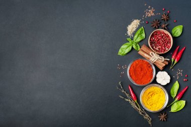 Çok renkli baharat zerdeçal, kırmızı biber, kekik tarçın, pembe biber, kekik, sarımsak gibi karanlık bir yüzeye fesleğen yaprağı. Metin için yer