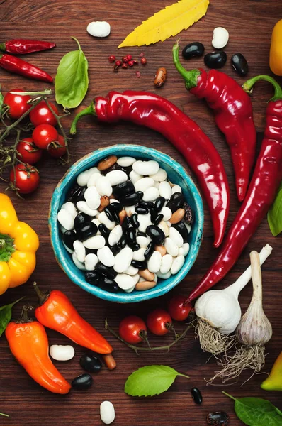 Πιάτο με πολύχρωμα φασόλια, επόμενη κόκκινες και κίτρινες πιπεριές, τοματίνια, σκόρδο και βασιλικό φύλλα. Ωμά λαχανικά. Συγκομιδή έννοια των τροφίμων — Φωτογραφία Αρχείου