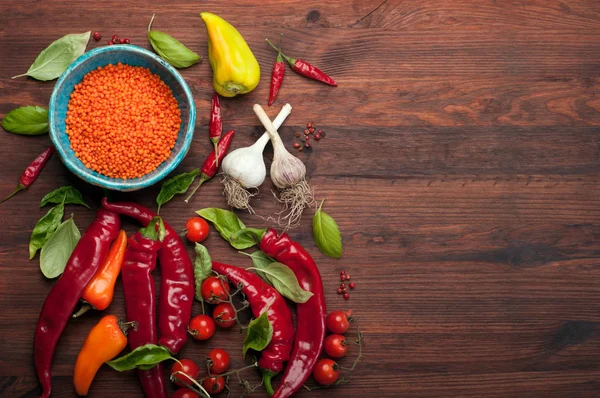 Prato com lentilhas vermelhas, perto das pimentas vermelhas, tomates cereja e folhas de manjericão. Legumes crus. Conceito de colheita de alimentos. Lugar para texto — Fotografia de Stock