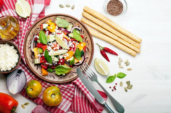 Salad dish made of tomatoes, peppers, cucumbers, purple onions, basil leaves, cottage cheese, olive oil and lime juice on a white background. A useful food. Healthy eating, balanced nutrition