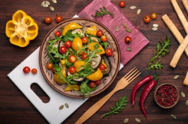 Akdeniz mutfağı. Sıcak fırında biber, patlıcan, roka yaprakları ve kahverengi kil tabakta domates salatası. Vegan kavramı. Diyet düşük kalorili yemek