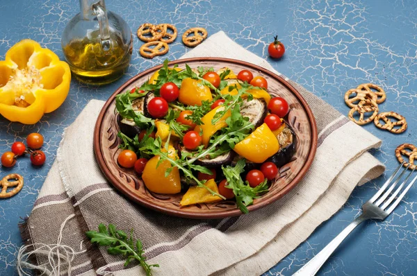 Mediterranean cuisine. Warm salad dish with baked pepper, eggplant, arugula leaves and cherry tomatoes on a brown clay plate. Vegan concept. Dietary low calorie food