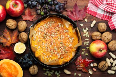 Sulu sarı kabak pasta kabak çekirdeği ve susam sonbahar yeşillik, elma, fındık ve üzüm arka planı ile dekore edilmiştir. Sonbahar mevsimlik menü. Vejetaryen kavramı