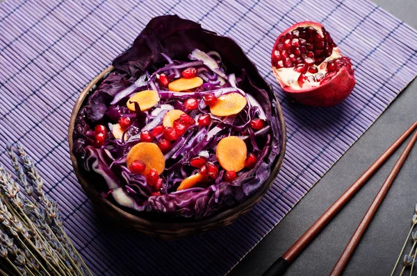 Dietary low-calorie salad of red cabbage, carrots, pomegranate seeds and olive oil in a plate on the background of a violet mat. Vegetarian, vegan concept — Stock Photo, Image