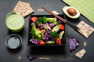 Brokoli, mor lahana, domates ve tatlı sosu ve karanlık bir arka plan üzerinde siyah bir kare tabak içinde zeytinyağı ile Avokado salatası. Yeşil smoothies ve soya sosu. Sağlıklı Diyet beslenme kavramı