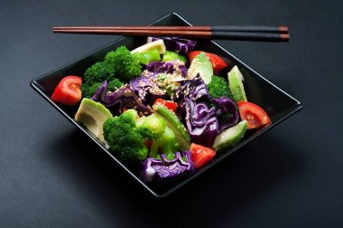 Brokoli, mor lahana, domates ve tatlı sosu ve karanlık bir arka plan üzerinde siyah bir kare tabak içinde zeytinyağı ile Avokado salatası. Sağlıklı Diyet beslenme kavramı