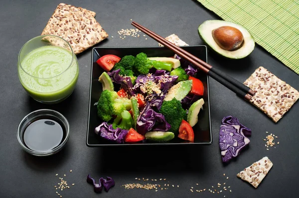 Brokoli, mor lahana, domates ve tatlı sosu ve karanlık bir arka plan üzerinde siyah bir kare tabak içinde zeytinyağı ile Avokado salatası. Yeşil smoothies ve soya sosu. Sağlıklı Diyet beslenme kavramı