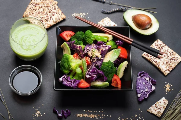 Brokoli, mor lahana, domates ve tatlı sosu ve karanlık bir arka plan üzerinde siyah bir kare tabak içinde zeytinyağı ile Avokado salatası. Yeşil smoothies ve soya sosu. Sağlıklı Diyet beslenme kavramı