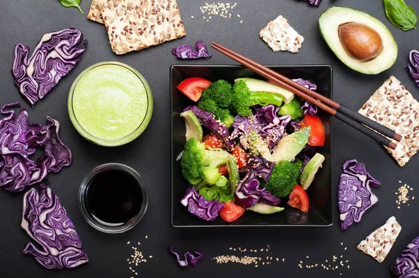 Brokoli, mor lahana, domates ve tatlı sosu ve karanlık bir arka plan üzerinde siyah bir kare tabak içinde zeytinyağı ile Avokado salatası. Yeşil smoothies ve soya sosu. Sağlıklı Diyet beslenme kavramı