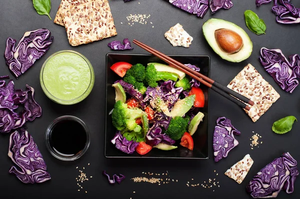 Brokoli, mor lahana, domates ve tatlı sosu ve karanlık bir arka plan üzerinde siyah bir kare tabak içinde zeytinyağı ile Avokado salatası. Yeşil smoothies ve soya sosu. Sağlıklı Diyet beslenme kavramı