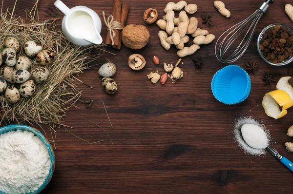 Un conjunto de productos para cocinar. Fondo culinario. Lugar para el texto. Harina, huevos de codorniz, nueces, pasas, especias y gadgets para cocinar sobre un fondo de madera marrón . — Foto de Stock