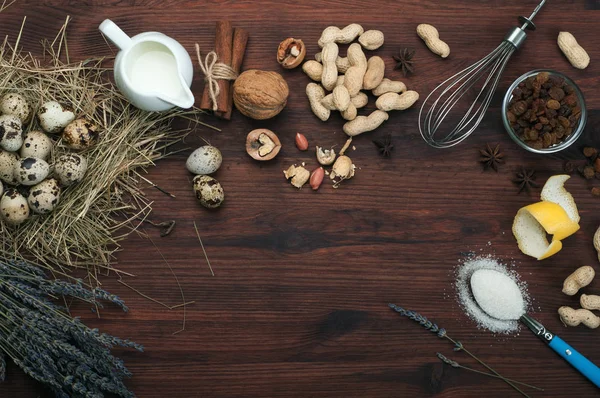 En uppsättning produkter för matlagning. Kulinariska bakgrunden. Plats för text. Grädde, vaktelägg, nötter, russin, kryddor och prylar för matlagning på brun trä bakgrund. — Stockfoto