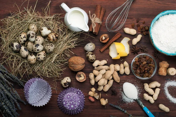 Um conjunto de produtos para cozinhar. Creme, ovos de codorna, nozes, passas, especiarias e gadgets para cozinhar em um fundo de madeira marrom . — Fotografia de Stock